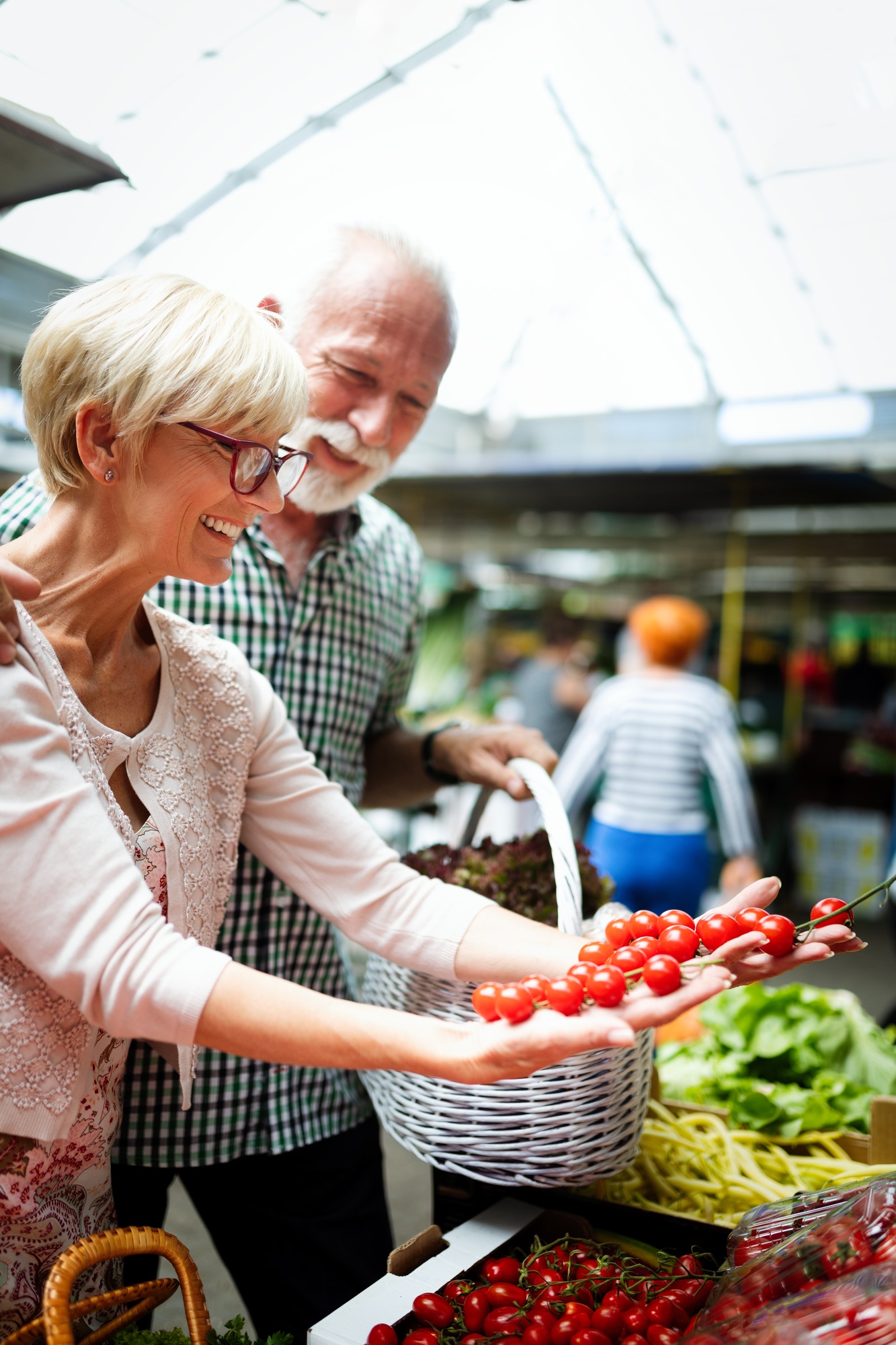Smiling senior couple holding basket with vegetables at the market