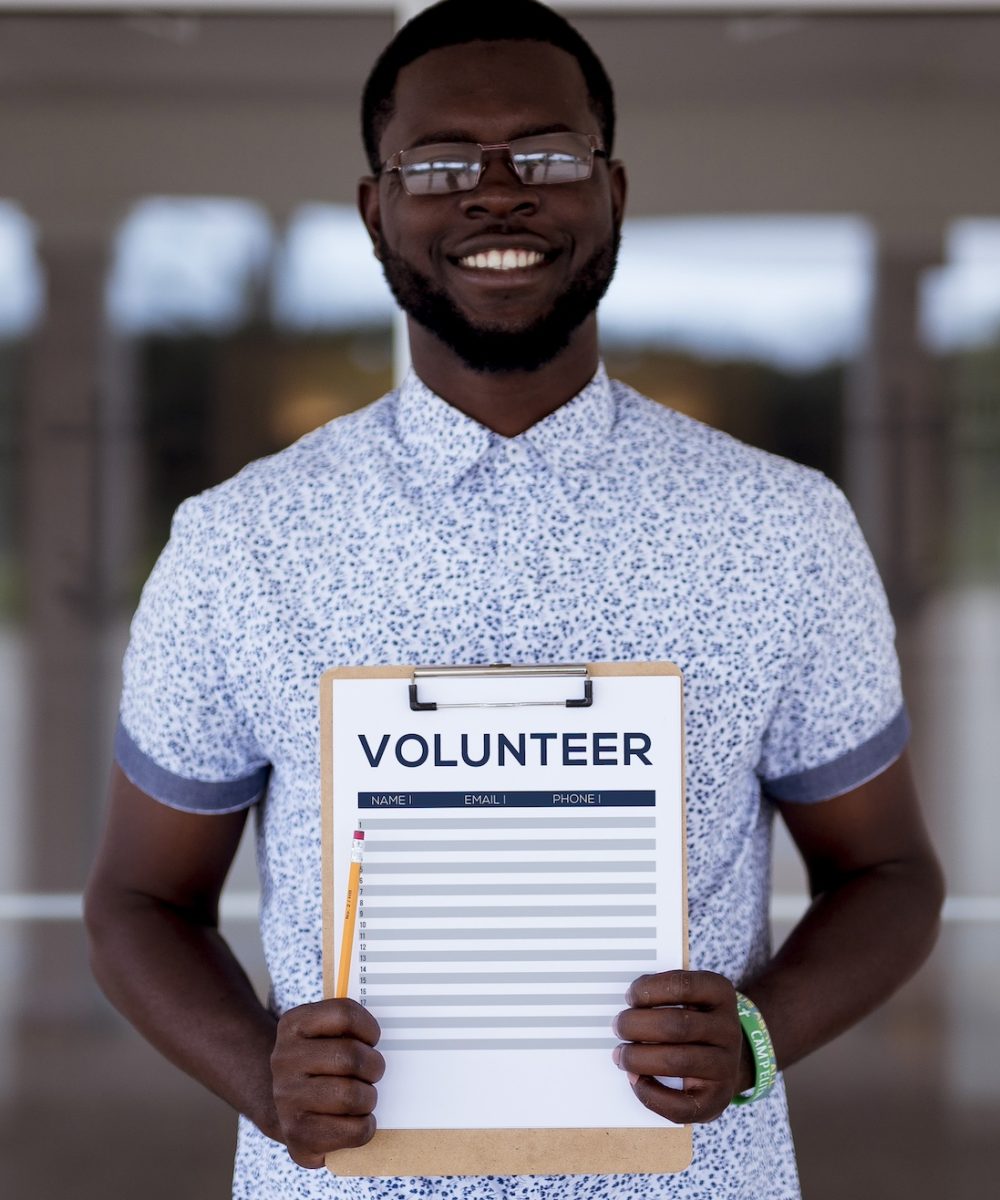 A vertical shot of a male holing a volunteer clipboard while smiling at the camera
